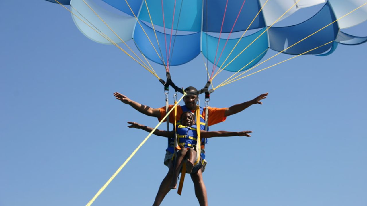 A child and an adult having fun parasailing together in the sky with Go Parasailing.
