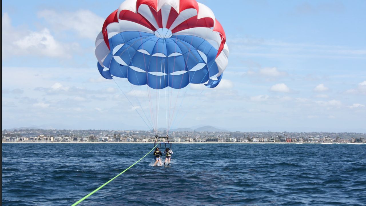 People parasailing under a red, white, and blue canopy above the ocean