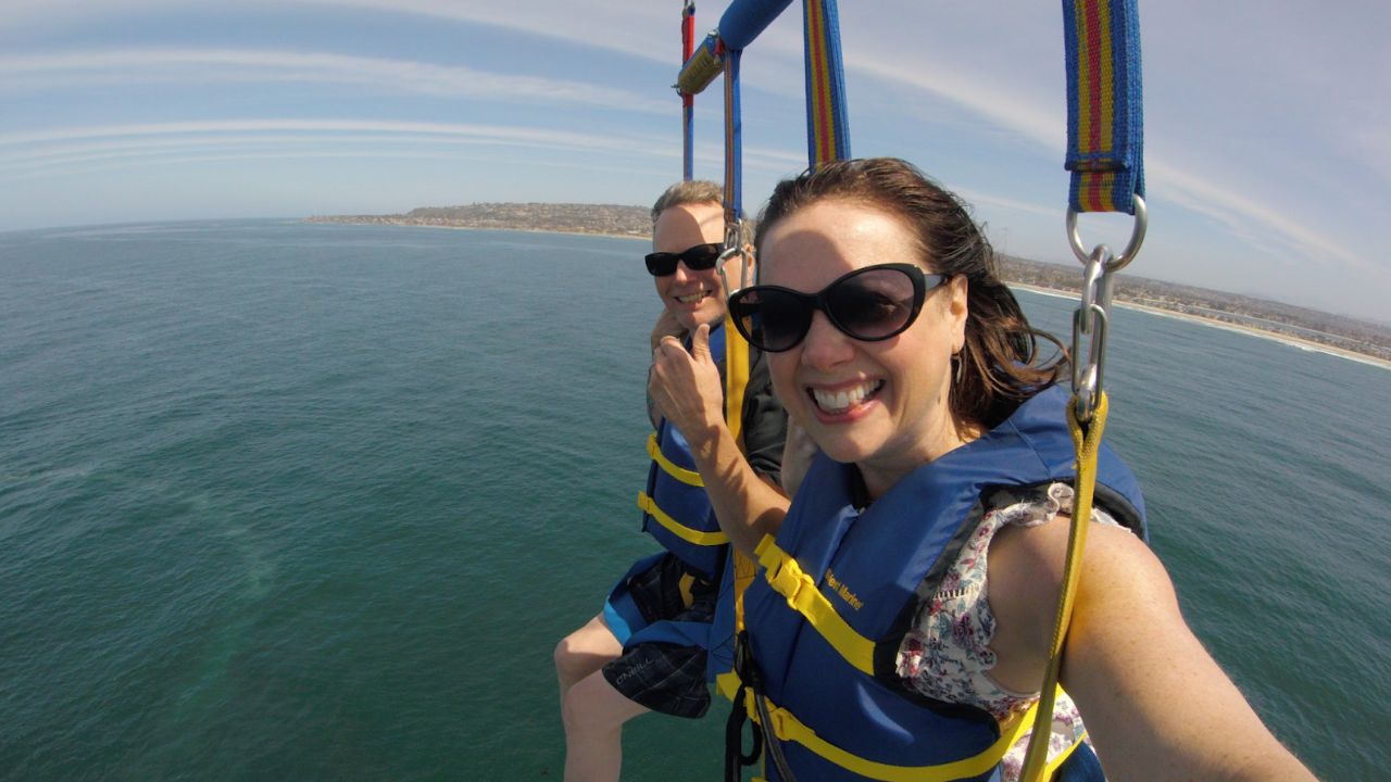 Couple parasailing high above the sea with coastline and clear sky