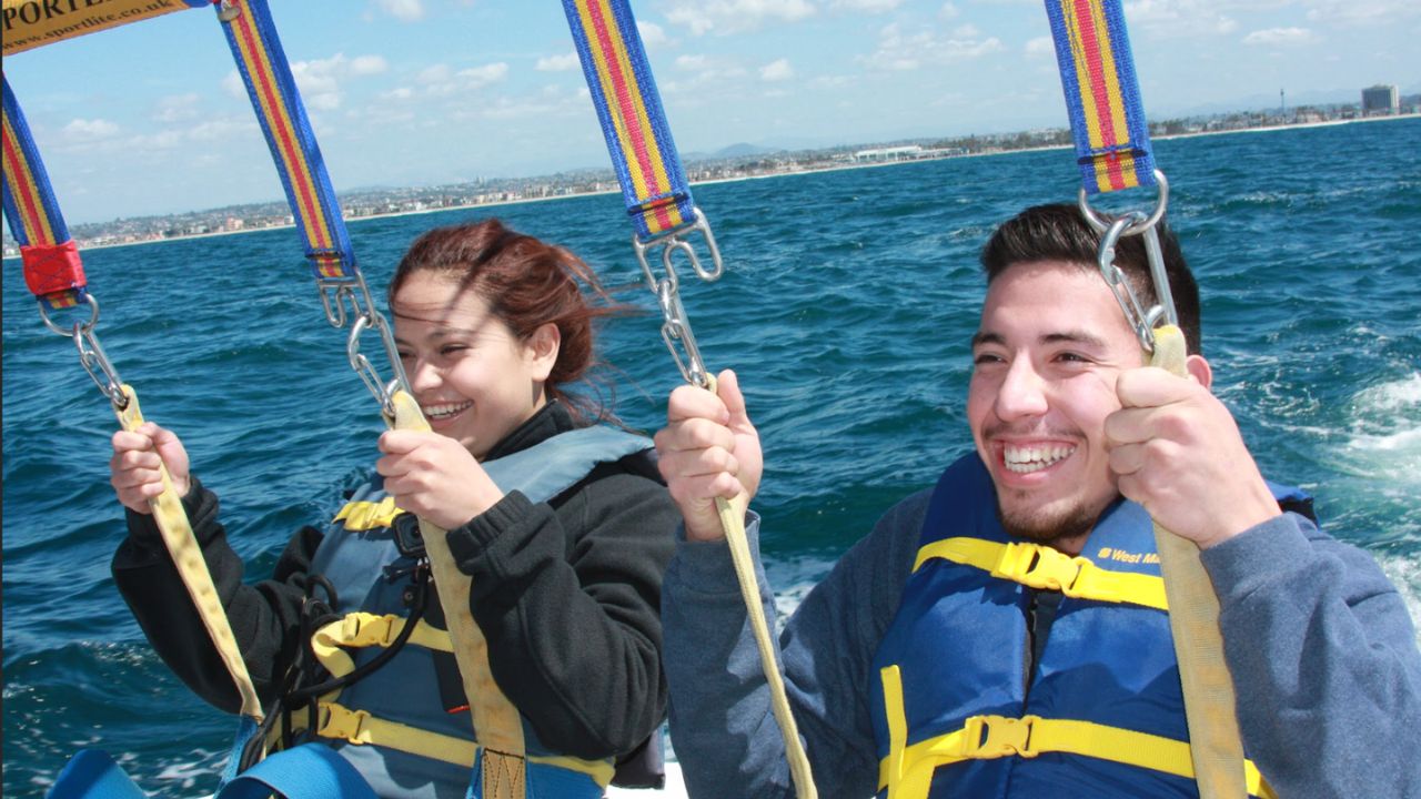 Two smiling riders in life jackets holding parasail straps over open ocean