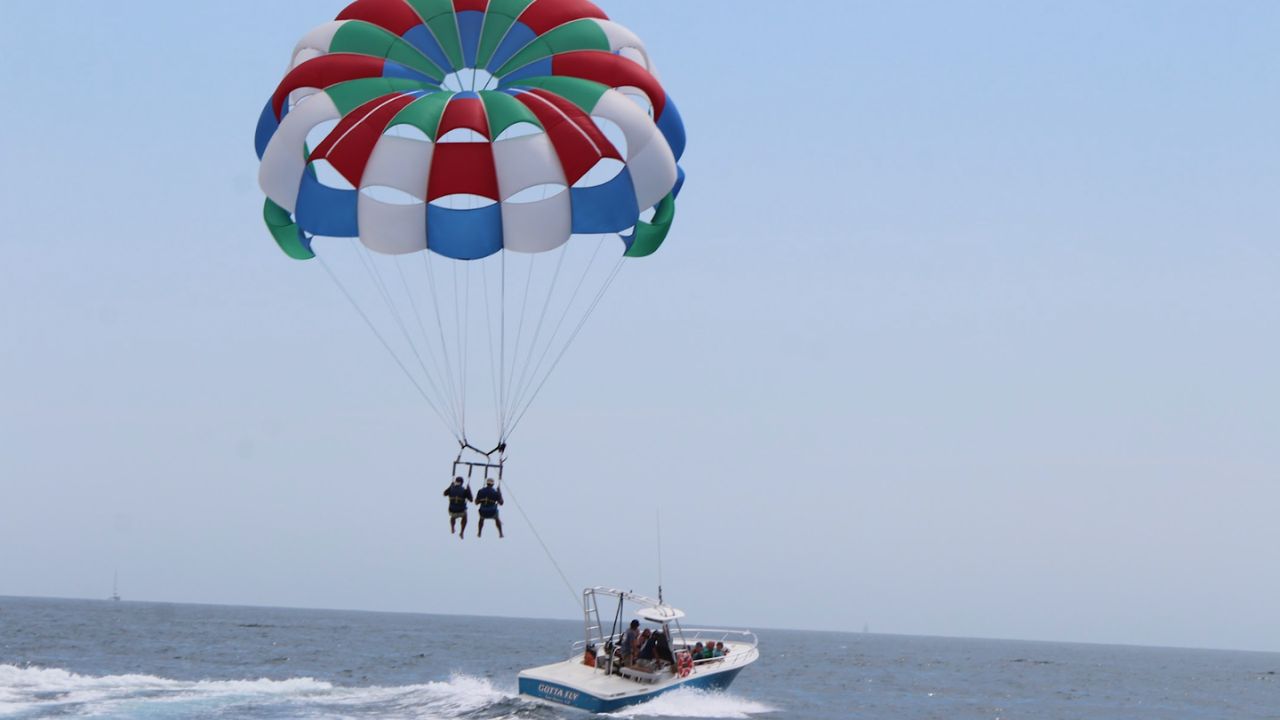 Colorful parasail canopy lifting two riders high above the ocean, pulled by a parasail boat below