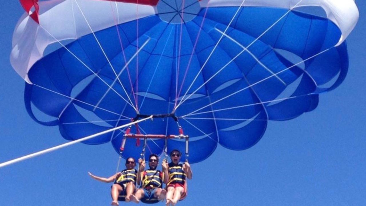 Three people enjoying parasailing ride with red blue parachute