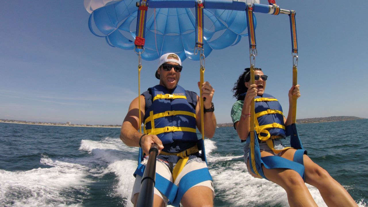 Couple enjoying parasailing adventure above sea with safety harness