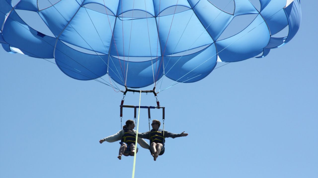 Two people parasailing high in the sky with parachute fully open. 