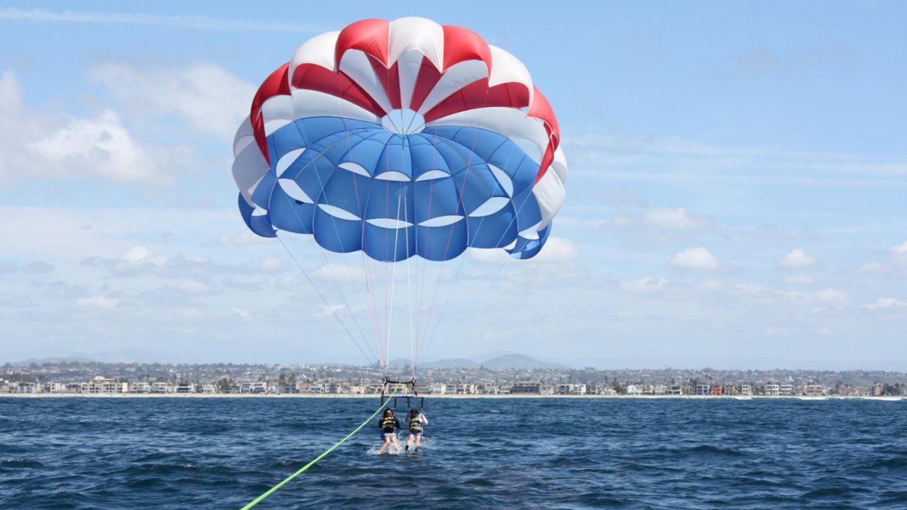 Parasail canopy over ocean with two riders being towed by boat near coastline. 