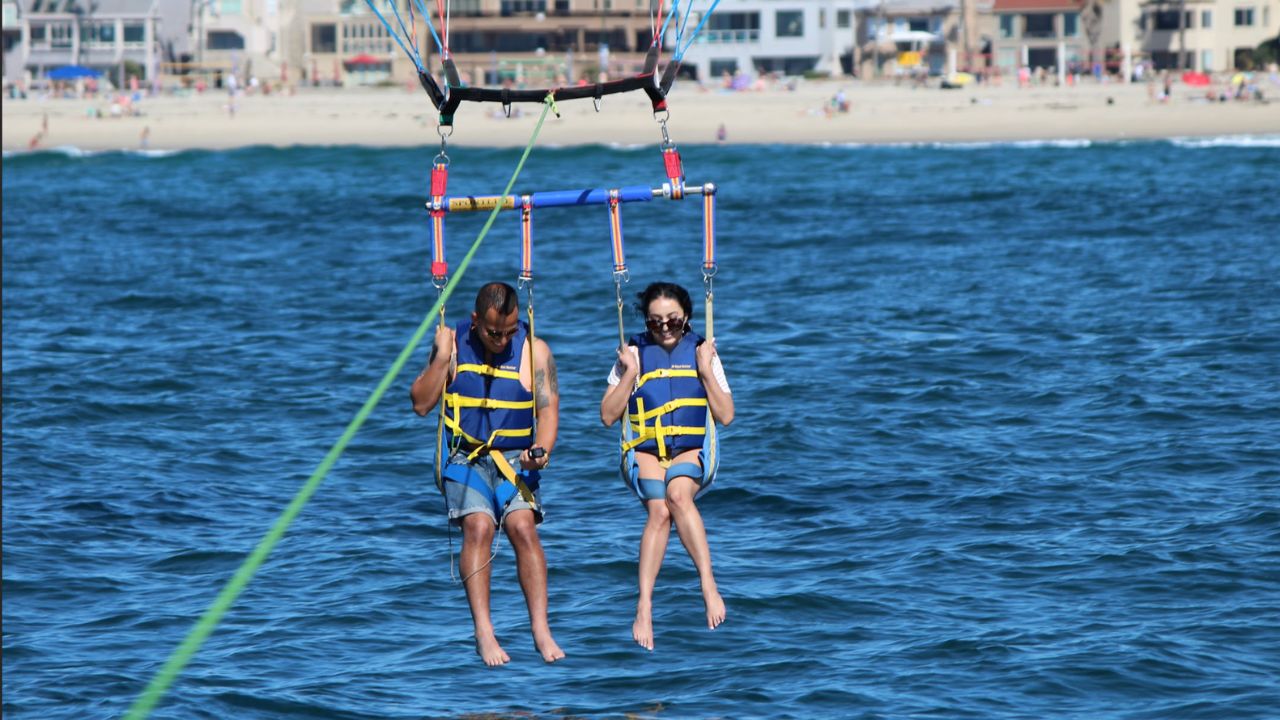 Couple parasailing close to shoreline with beach houses in background