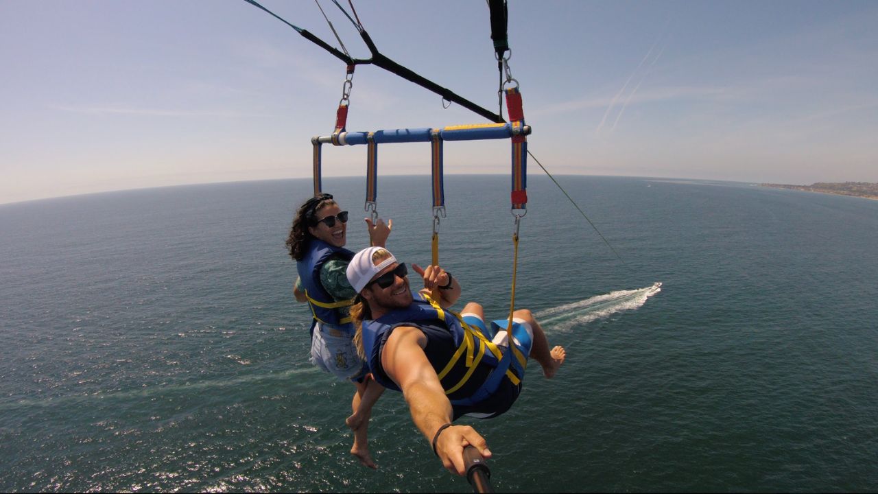 Couple enjoying a tandem parasailing flight with breathtaking views of the Pacific Ocean.