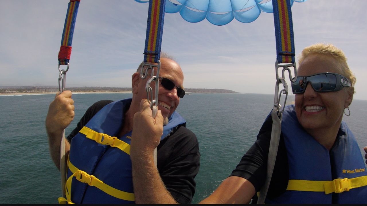 Couple enjoying a tandem parasailing flight with panoramic ocean views over San Diego Bay.