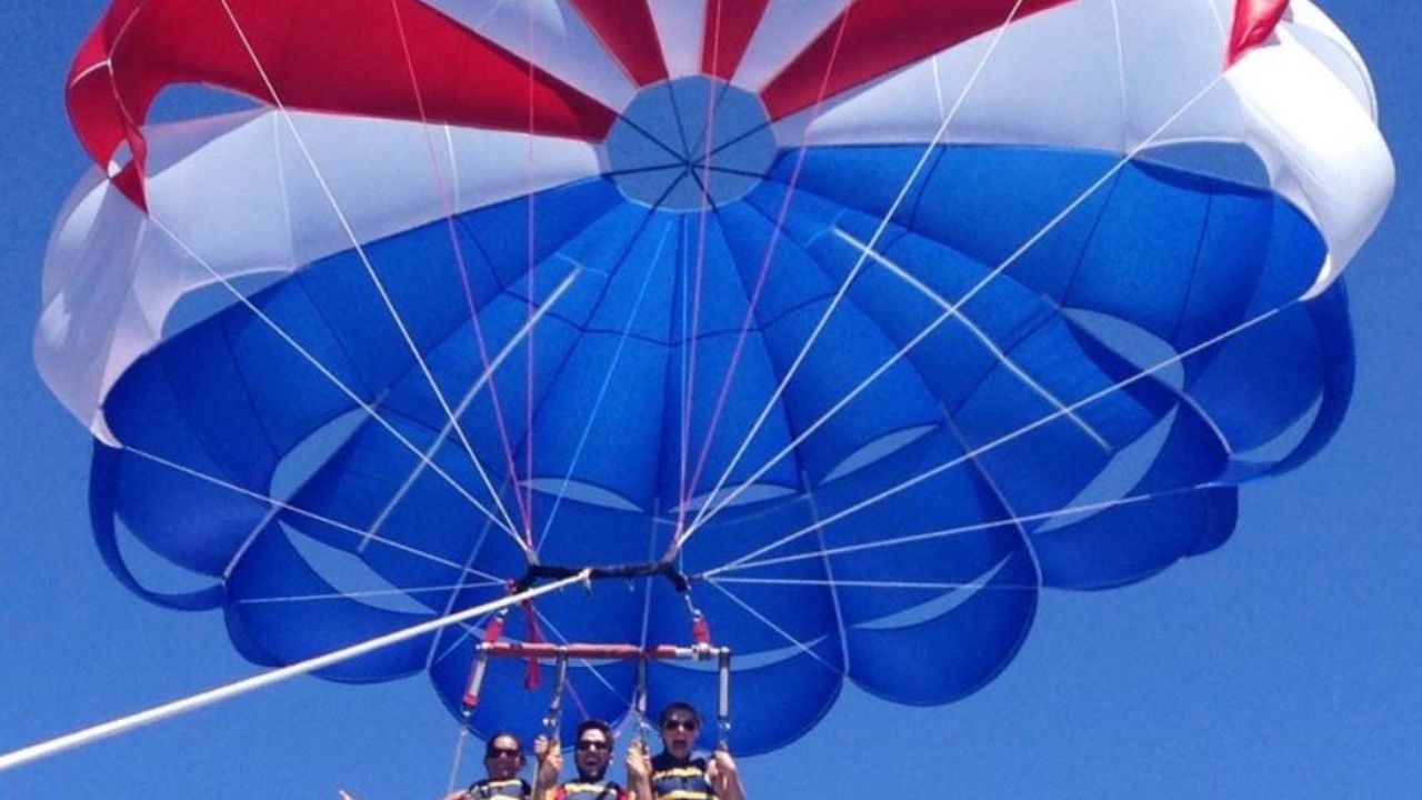Three people parasailing together under a red, white, and blue parachute over the ocean.