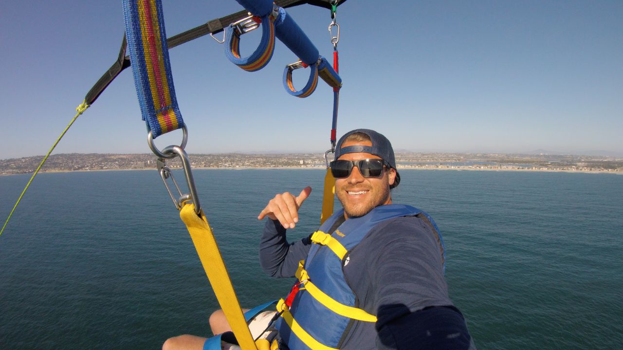 Parasailer enjoying panoramic ocean and coastline views while securely harnessed during a San Diego parasailing experience. 
