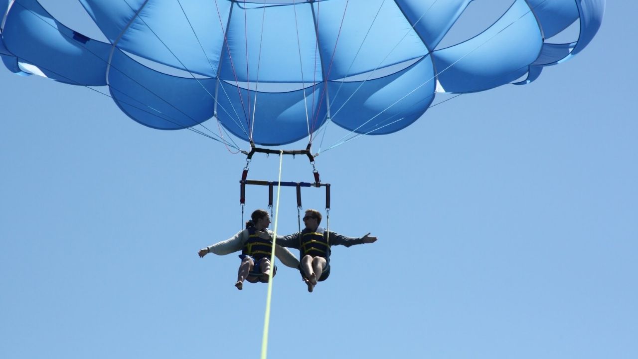 Two people enjoying a tandem parasailing experience high above the water.