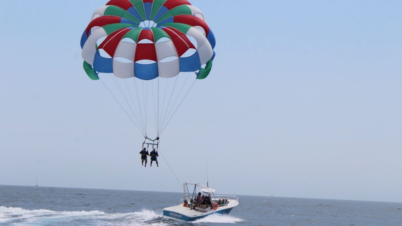 Two parasailers soaring above the ocean behind a speeding boat. 