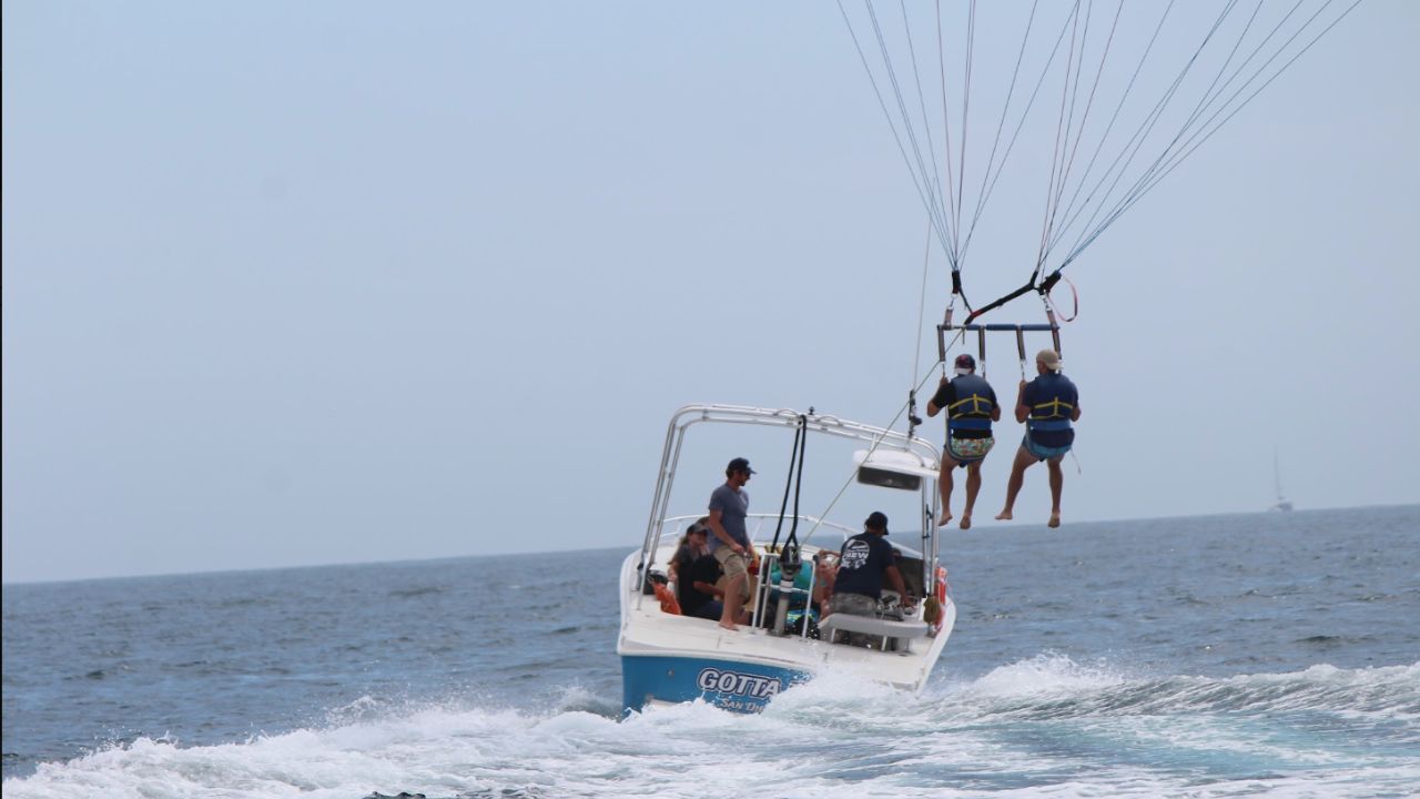 Two guests lifting off from a parasail boat during a tandem parasailing experience over the Pacific Ocean.