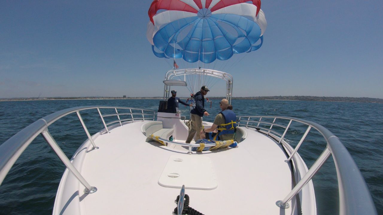 Parasailing crew preparing a guest aboard a boat beneath a colorful parachute on the San Diego coast.