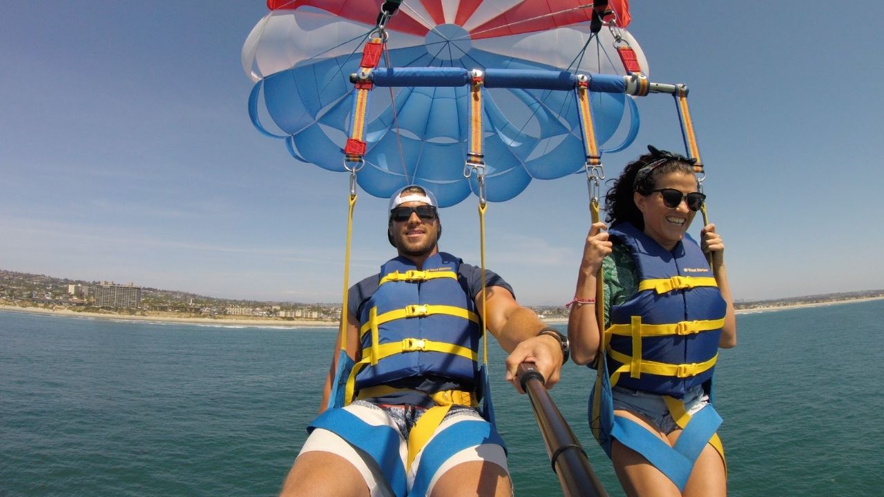 Two people enjoying tandem parasailing with scenic coastal views.